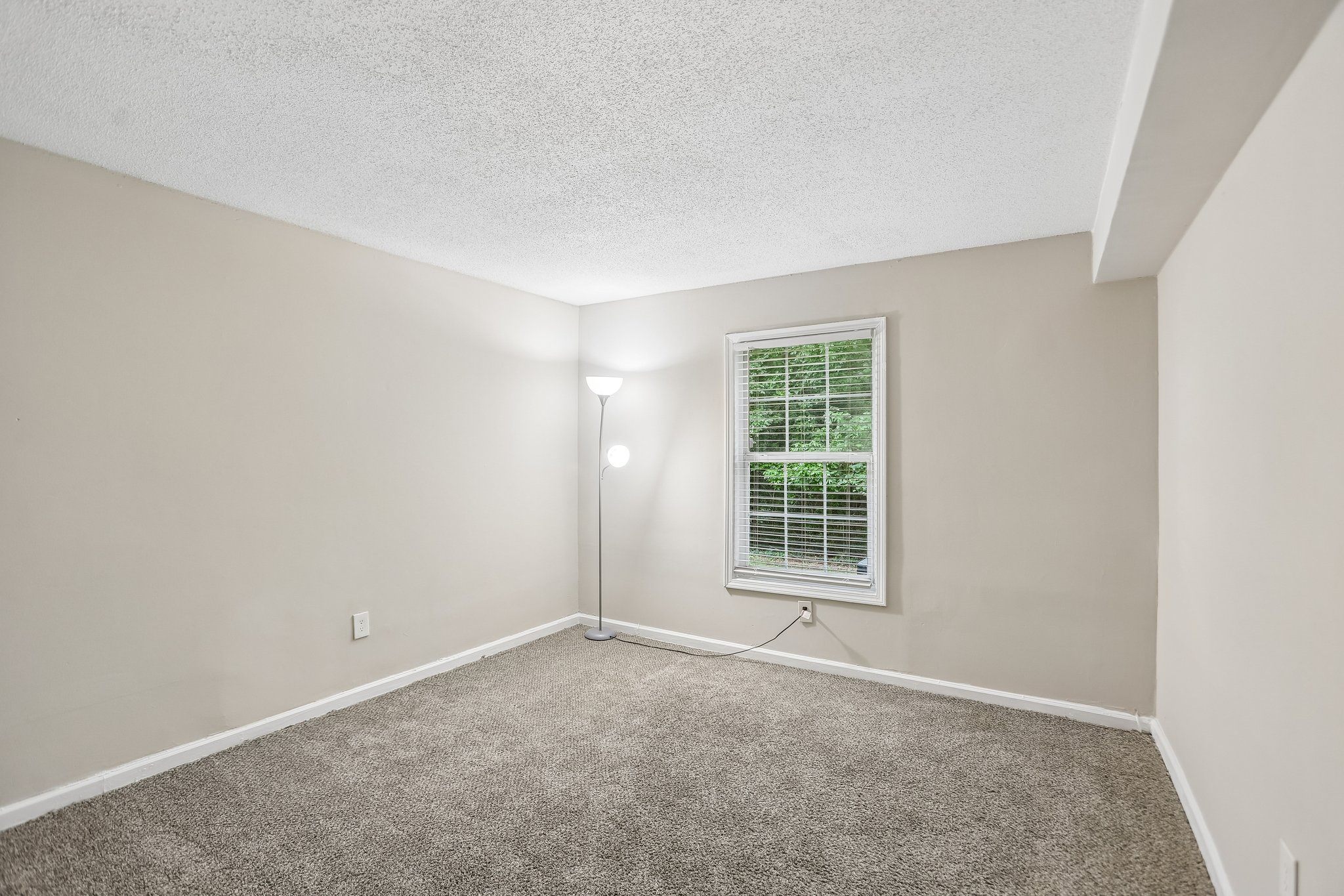 A room with a carpeted floor and a window with blinds.